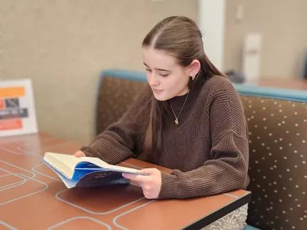 A girl reading a book while sitting at a table, embodying concentration and tranquility in her surroundings.