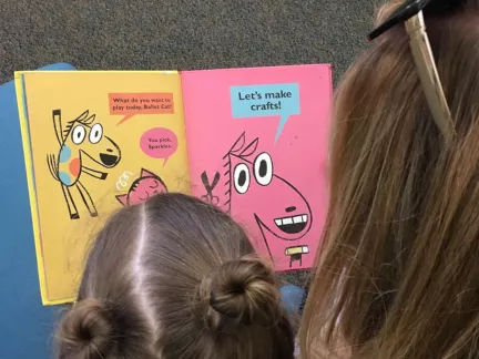 A woman and a child are engaged in reading a book together, featuring a story about a dog.