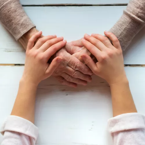 young person's hands covering a older adult's hands that are clasped