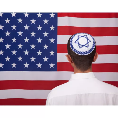 A man with a white yamaka standing in front of an American Flag